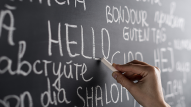 A person writing the word 'hello' amongst other languages on a blackboard.
